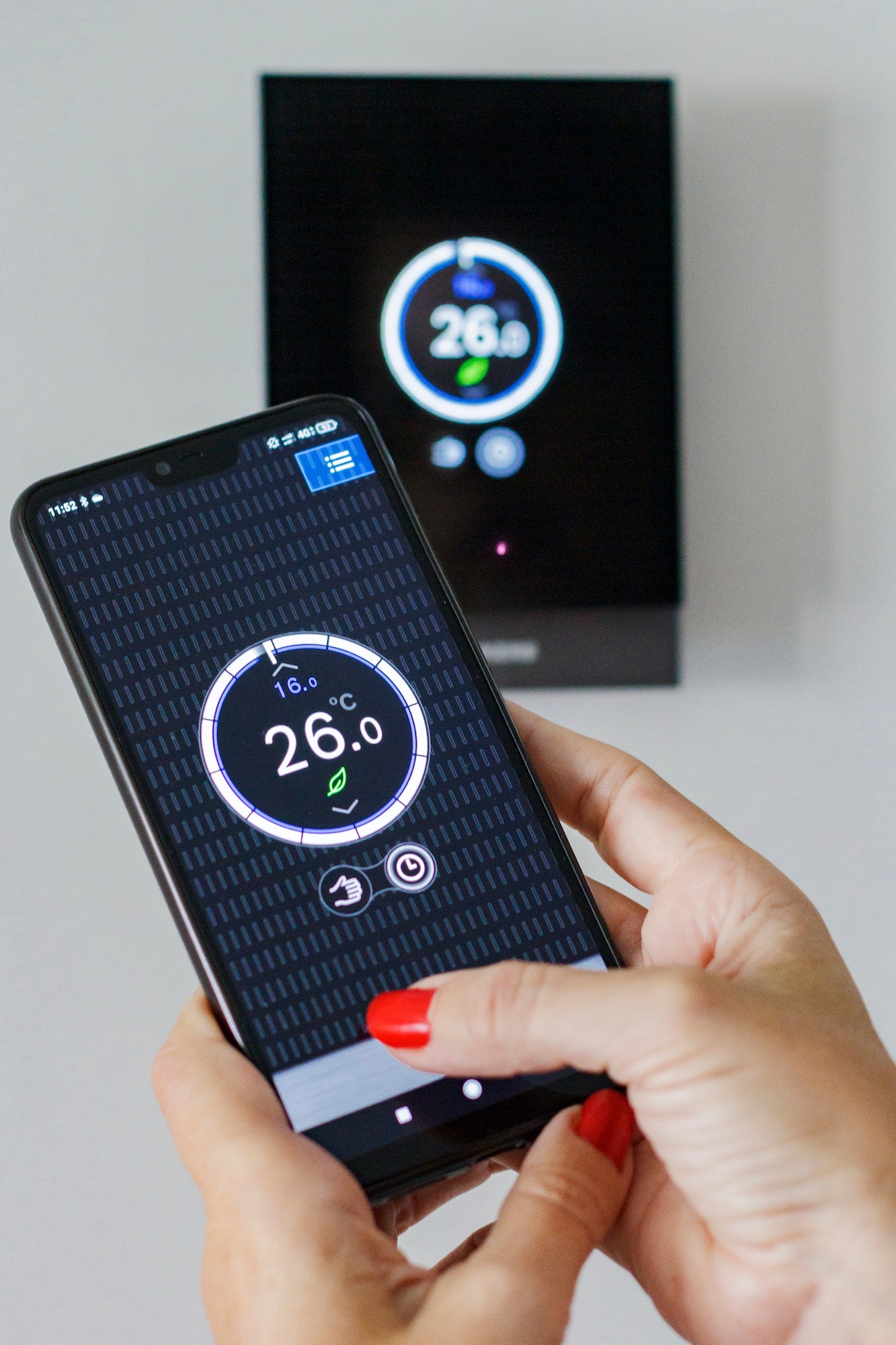 Female hands controlling via app on mobile phone the temperature in a thermostat at home, wireless